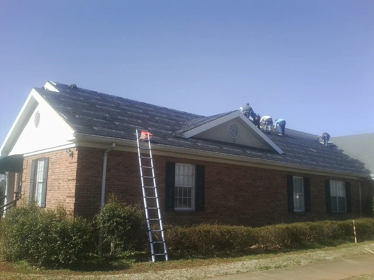 Crew tearing shingles off a brick ranch roof with a ladder set — Metal Roof Repair work by our crew in Tahuya