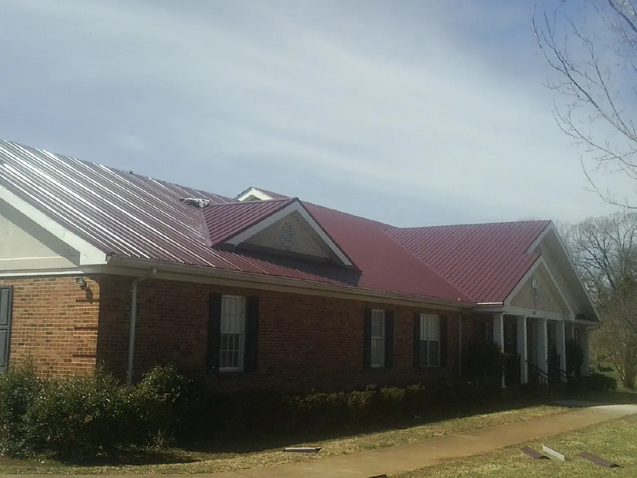 Red metal roof with gabled entries on a long brick building, from a Hail Damage Roof Repair job in Tahuya