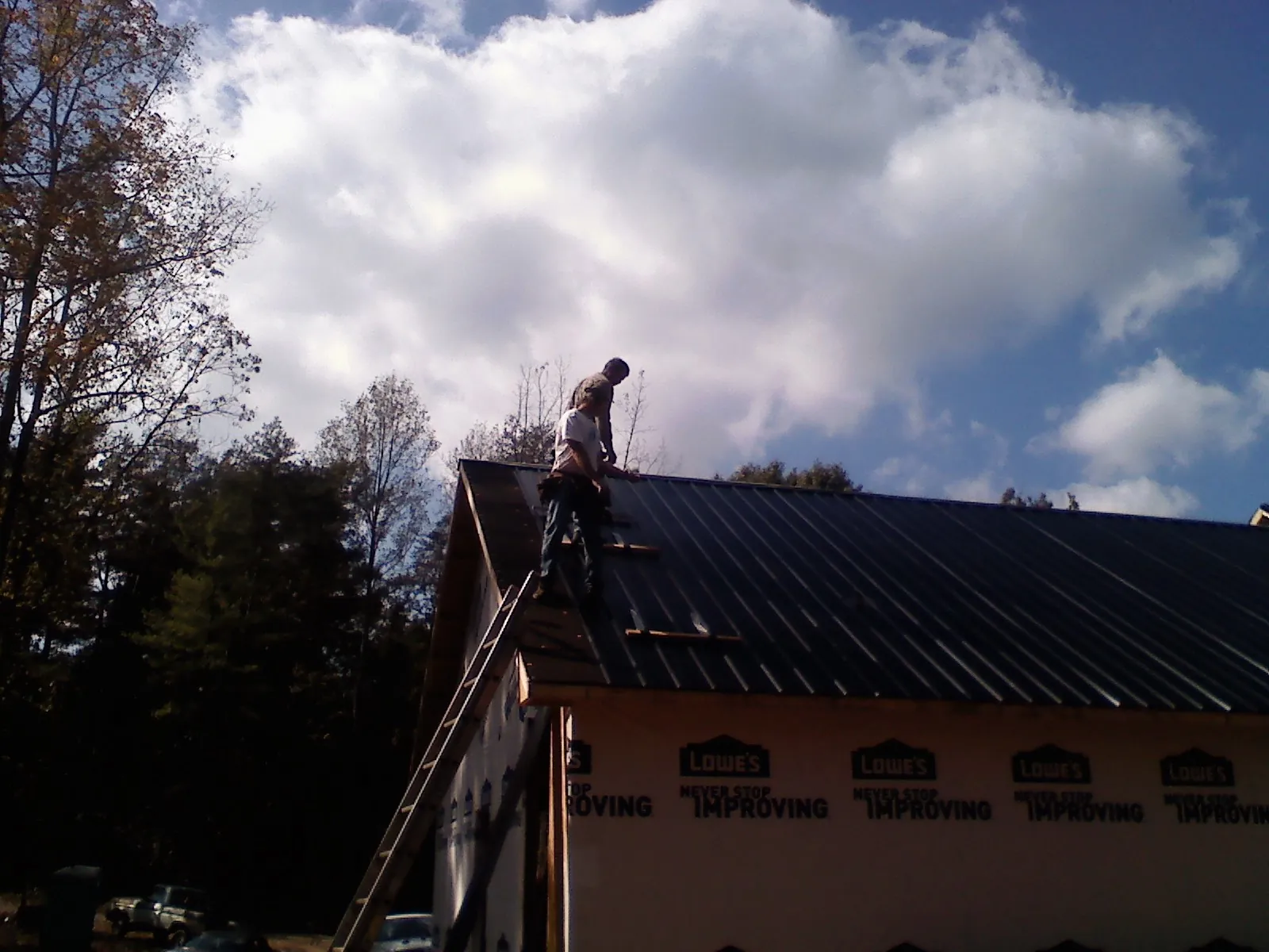 Roofer fastening dark metal panels high against a cloudy sky, from a Roof Inspection job in Tahuya