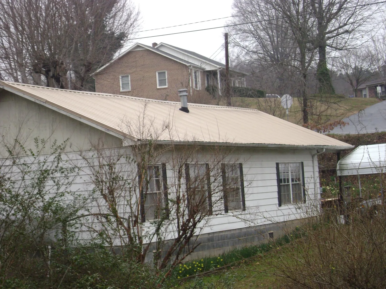Tan metal roof on a white sided house set into a hillside — Commercial Roofing by Roofing Brothers in Tahuya